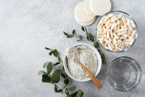 Closeup Collagen For Preparing A Cosmetic Mask In Ceramic Bowl With Spoon And Capsules For Diet Food, Loofah Sponges And Dry Eucalyptus Branches On Old Gray Concrete Background. Flat Lay With Copy Space.