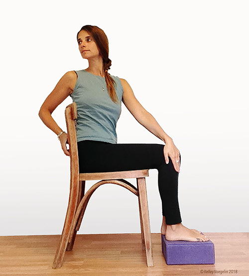 Seated spinal twist yoga pose can be modified for people with limited mobility. woman doing seated spinal twist yoga pose modification in chair