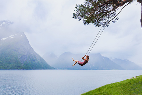 Daydreaming lets us become receptive to a broader range of experiences. woman swinging in beautiful daydream setting of water and mountains